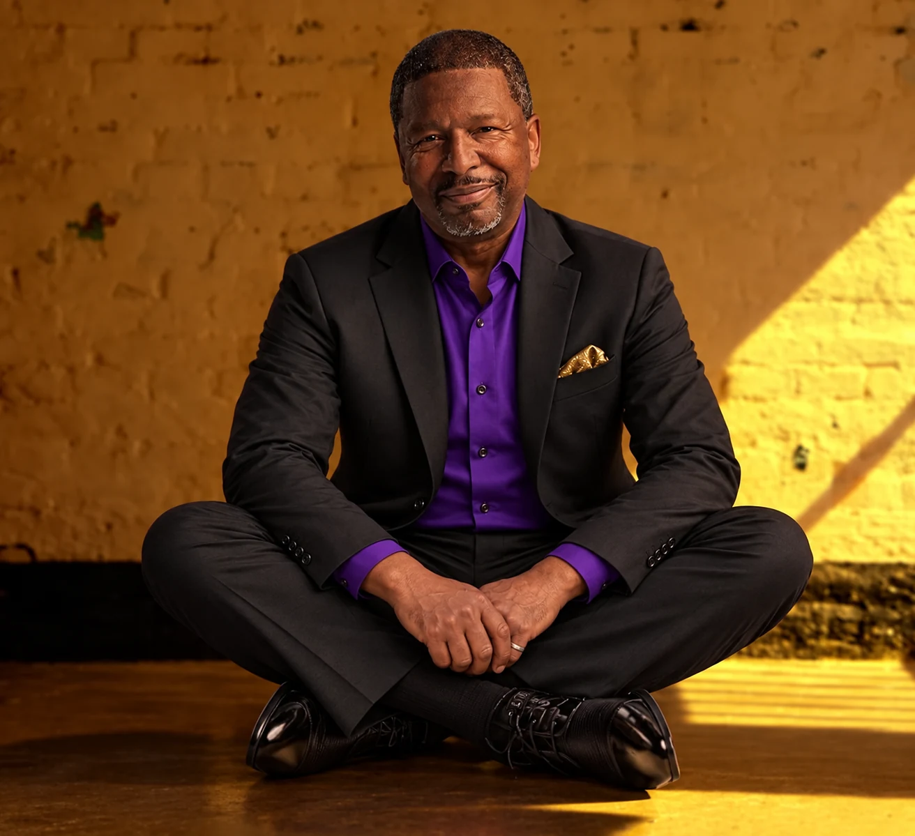 Avery Kyle wearing a black suit, purple shirt, and gold pocket square